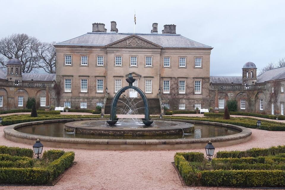 A large historic building with a central fountain and well-manicured gardens.