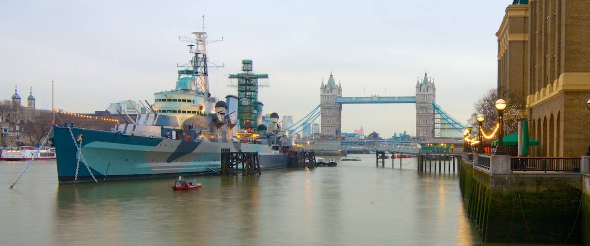 A large naval ship docked at a pier with the Tower Bridge in the background.