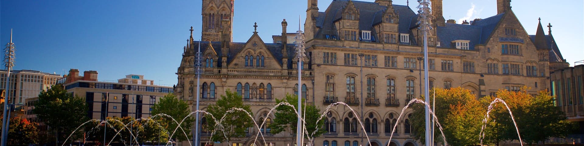A historic building with a clock tower, a fountain, and surrounding trees.