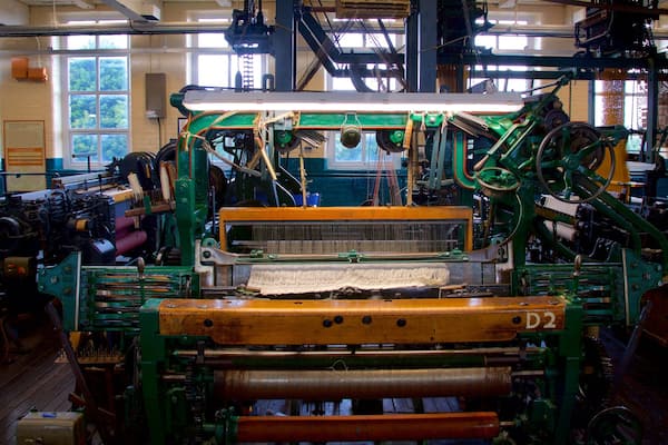 Un grand métier à tisser industriel aux éléments verts et orange, installé dans une pièce spacieuse dotée de grandes fenêtres.