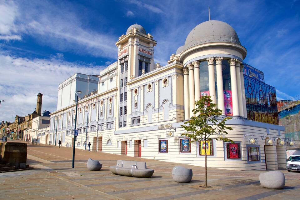 A historic building with columns and a dome, surrounded by a plaza with benches and a tree.