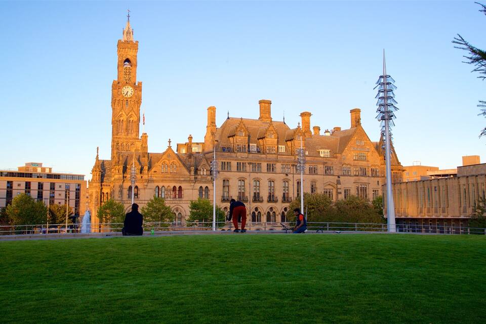 A historic building with a clock tower, surrounded by a grassy area and modern structures.