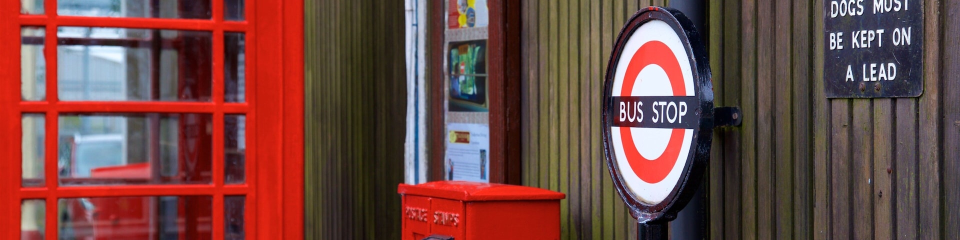 A red telephone booth, a bus stop sign, and a sign instructing dogs to be kept on a lead.