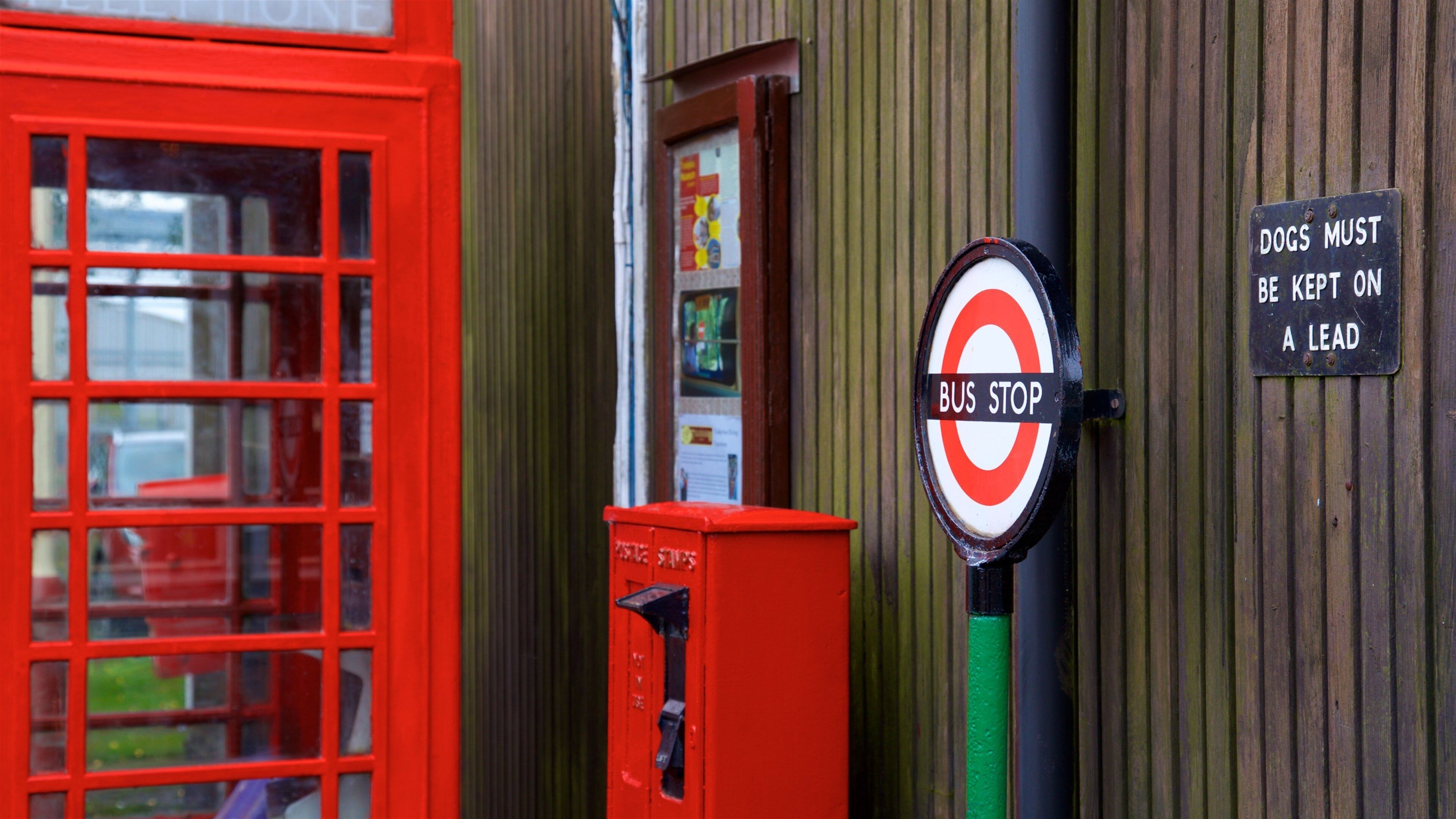 A red telephone booth, a bus stop sign, and a sign instructing dogs to be kept on a lead.