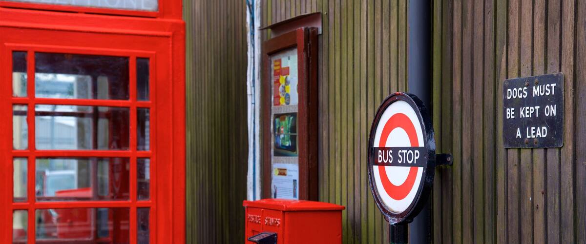 A red telephone booth, a bus stop sign, and a sign instructing dogs to be kept on a lead.