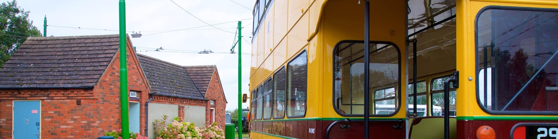 A yellow double-decker bus at a station with a brick building and a bench in the foreground.