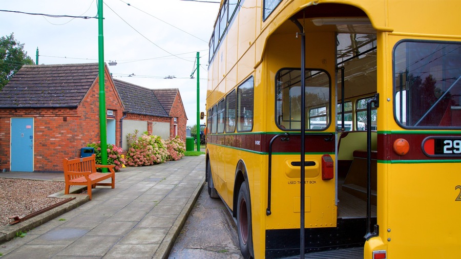 A yellow double-decker bus at a station with a brick building and a bench in the foreground.