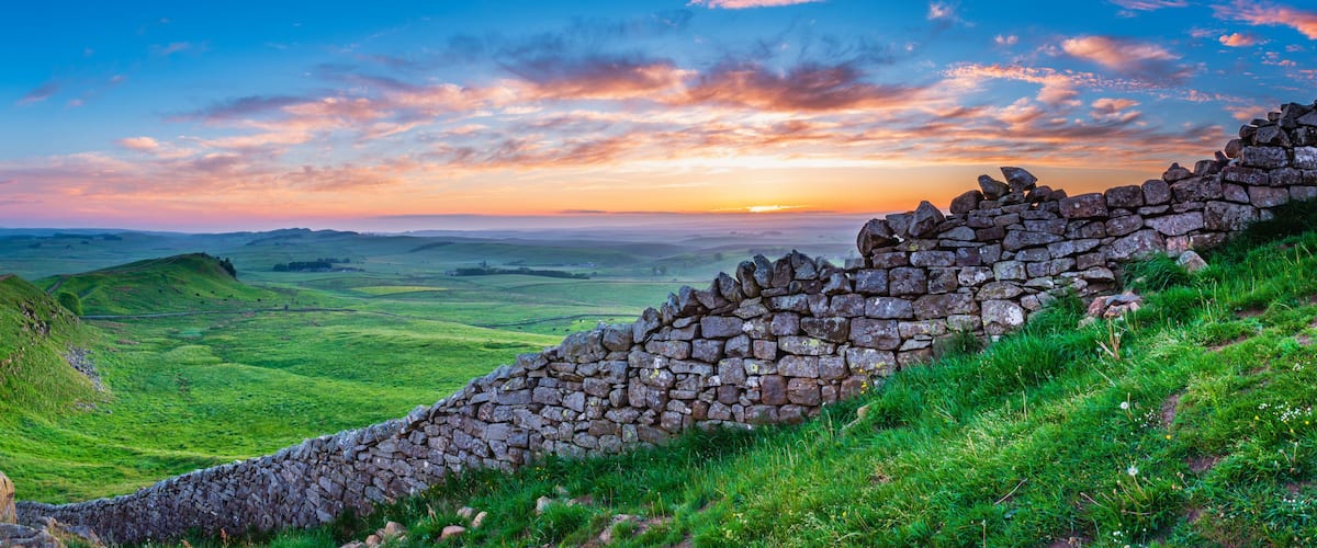 A stone wall, rolling hills, and a sunset over a green landscape.