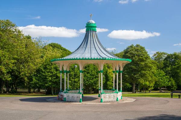 A gazebo with a green and white color scheme, surrounded by trees and a clear sky.