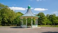 Un kiosque aux couleurs vert et blanc, entouré d’arbres et sous un ciel dégagé.