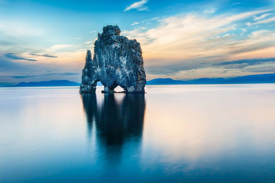A rock formation in a calm body of water with a clear sky.