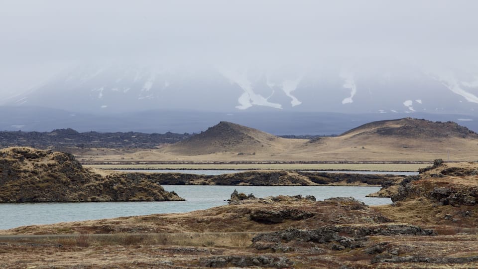 A rugged landscape with a body of water, rocky terrain, and distant snow-capped mountains.