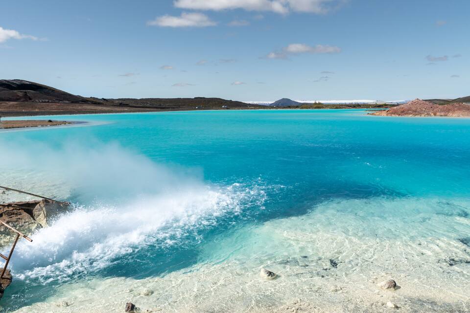 Um lago azul-turquesa com águas límpidas, rodeado por colinas e uma montanha ao longe.