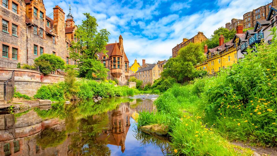A historic town with a river, stone buildings, and lush greenery.