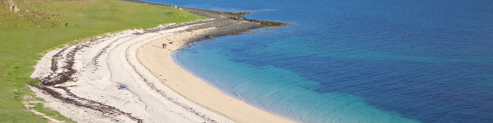 Paisagem costeira com uma praia de areia, linha costeira rochosa e uma cadeia montanhosa ao longe.