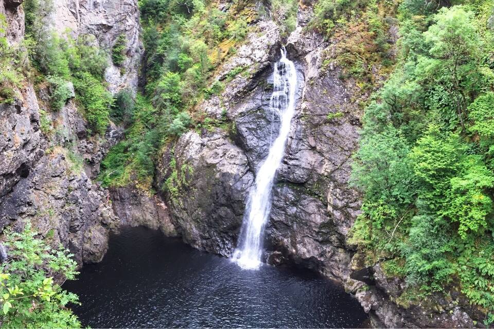 A waterfall cascading into a dark pool surrounded by lush green vegetation.