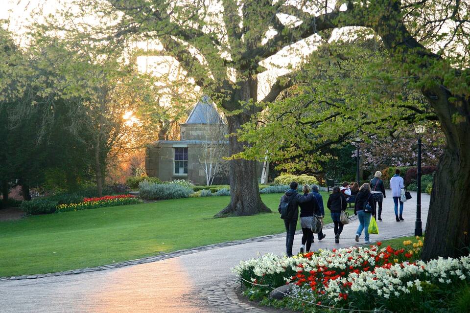 Un sentier bordé de fleurs et d’arbres, qui mène à un bâtiment doté d’une tour.