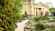 A garden with a stone pathway, lush greenery, and a historic building with columns.