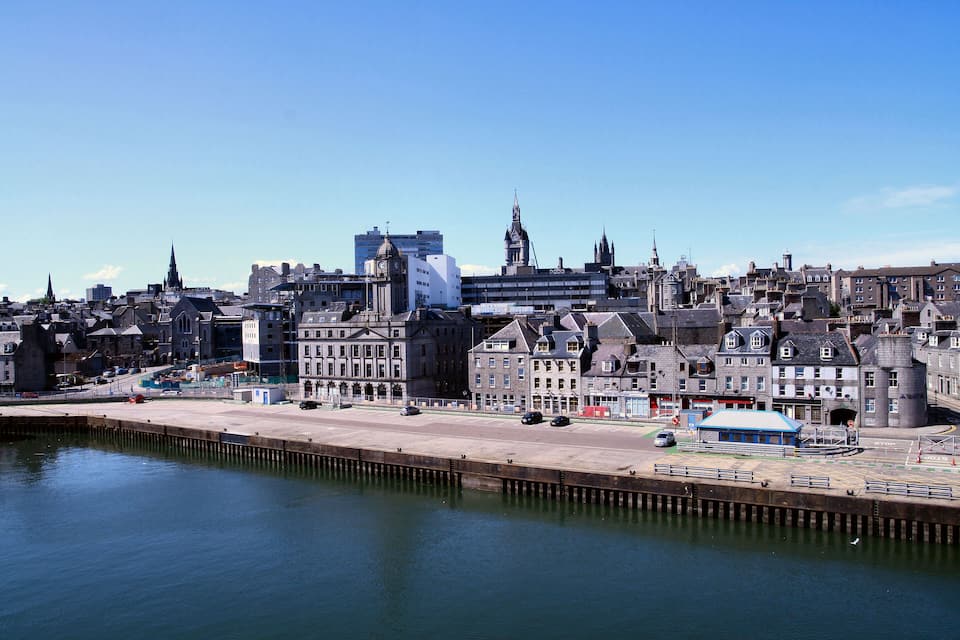 A coastal cityscape with historic buildings, a prominent church, and a modern skyscraper.