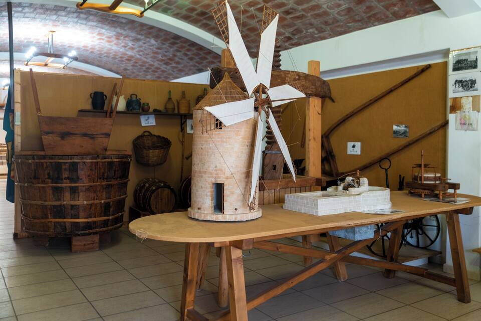 A windmill with wooden sails, a wooden table, and barrels in a rustic setting.