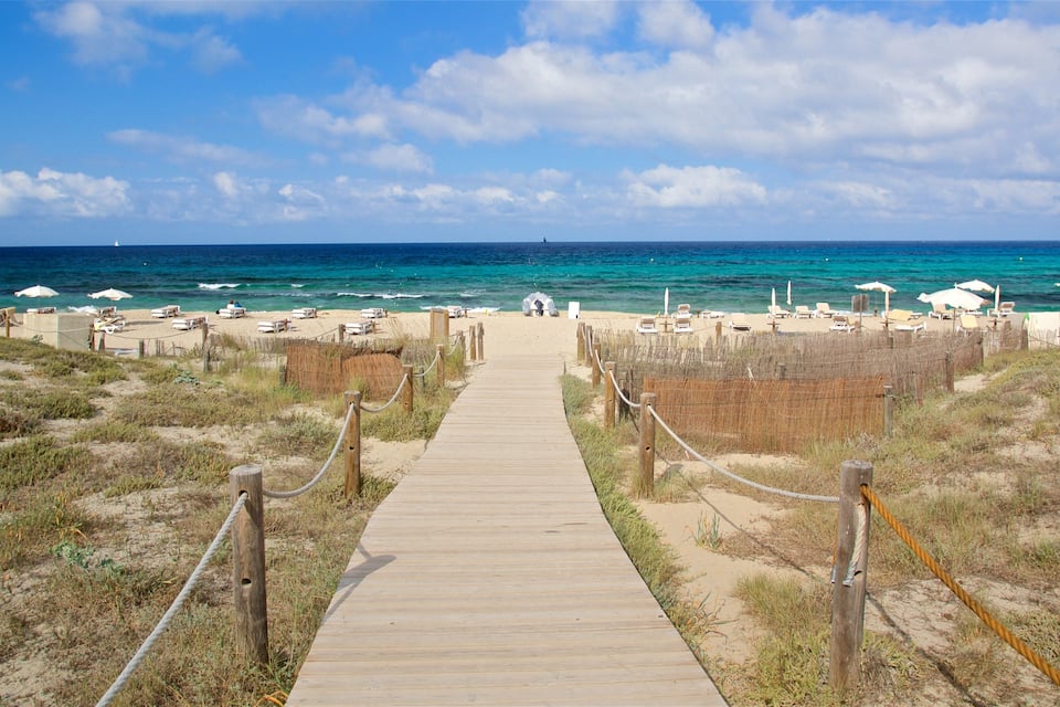 A wooden boardwalk leading to a beach with white umbrellas and lounge chairs.