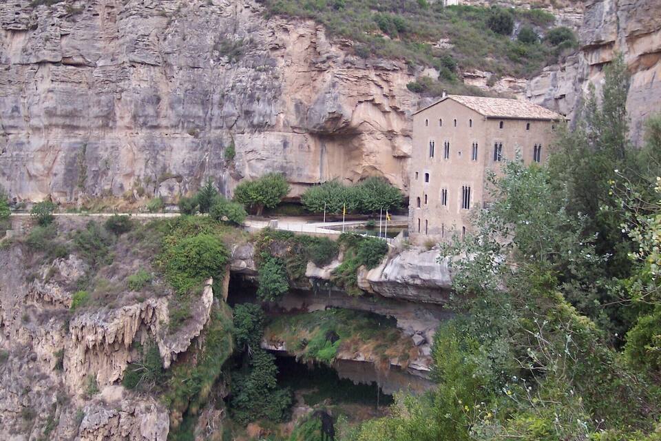 A building nestled in a rocky gorge with lush greenery and a steep cliff face.