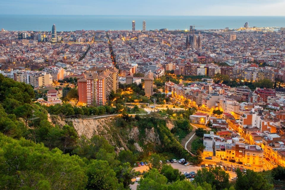 Un paisaje urbano costero con edificios densos, una torre destacada y un terreno montañoso con vegetación.