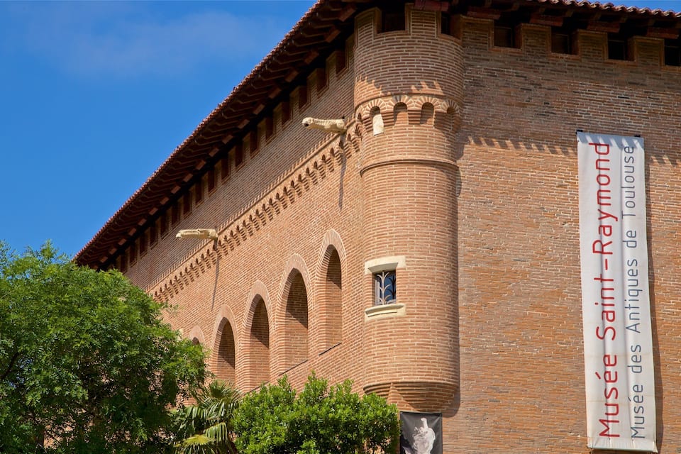 Un edificio de ladrillo con ventanas arqueadas y un letrero que dice 'Musée Saint-Raymond'.