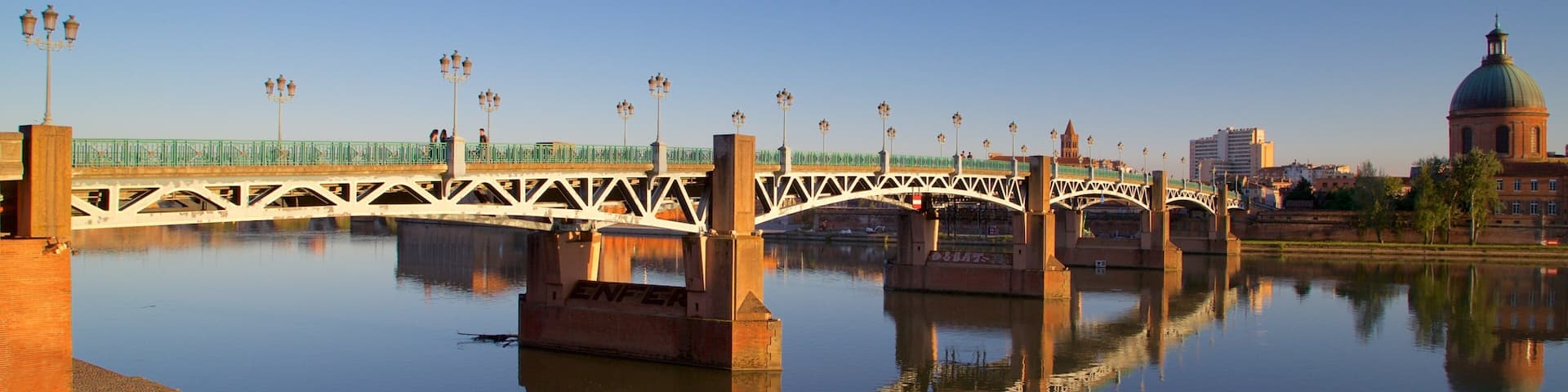 A river with a bridge, a calm water surface, and a dome structure in the background.