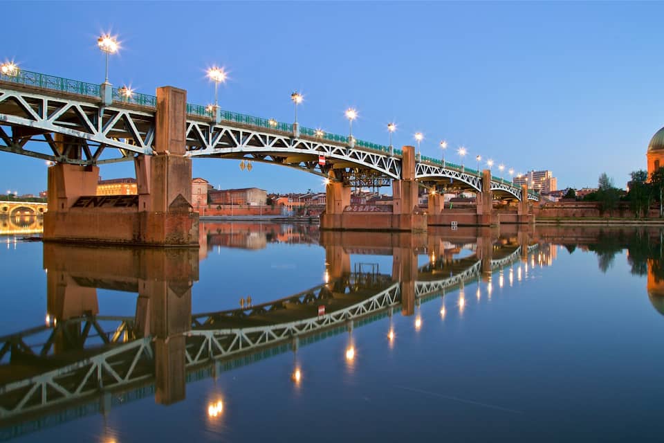 A bridge with lights reflecting on the water, a dome-shaped building, and a calm river.