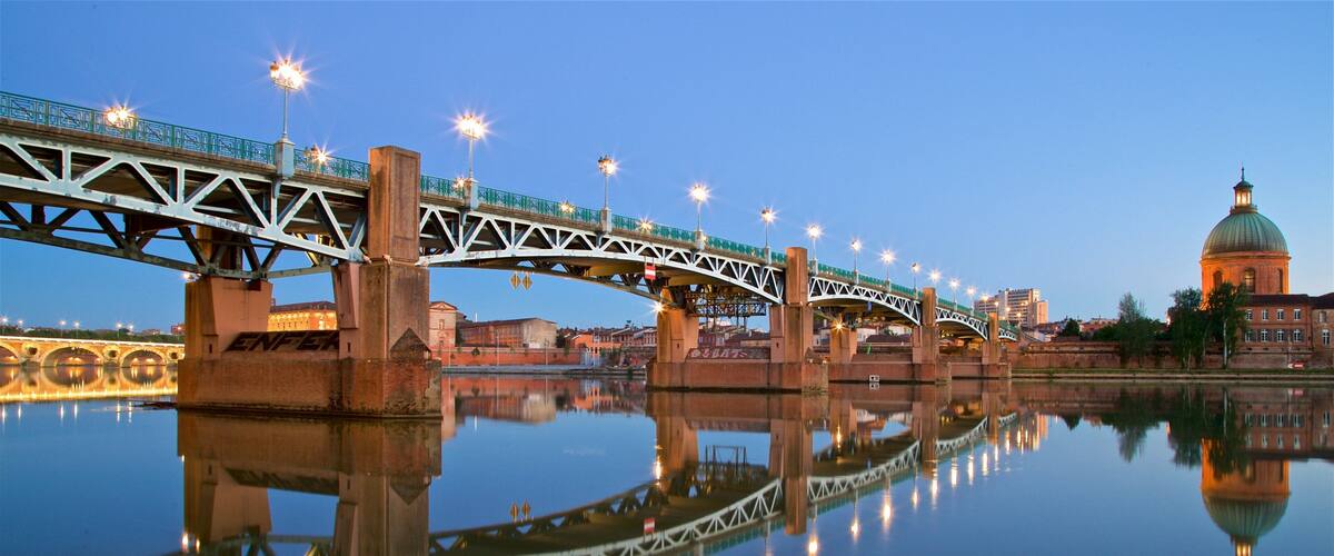 A bridge with lights reflecting on the water, a dome-shaped building, and a calm river.