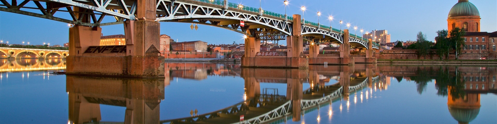 A bridge with lights reflecting on the water, a dome-shaped building, and a calm river.