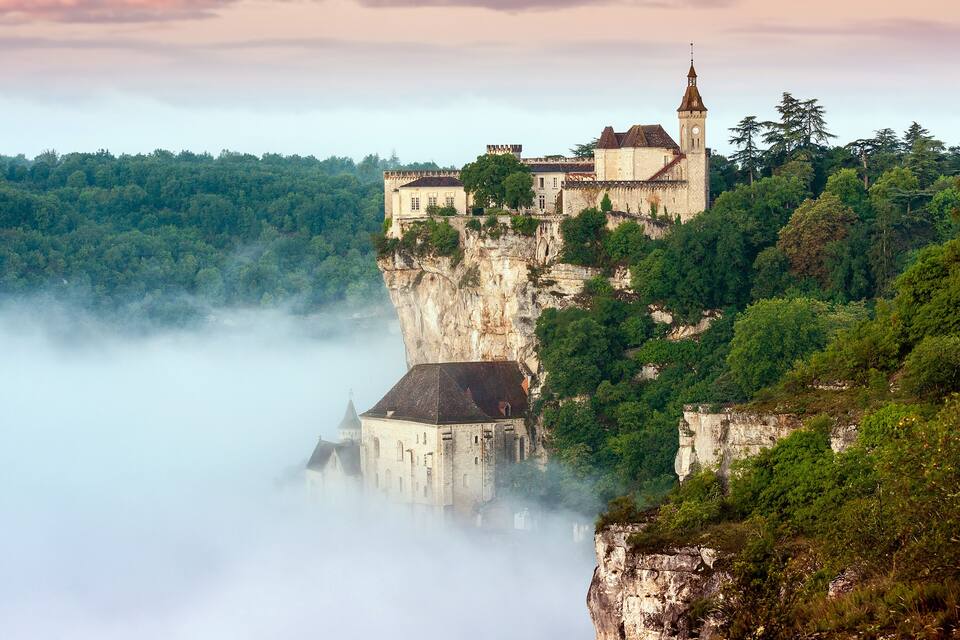 Un château perché au sommet d’une falaise, surplombant une vallée boisée.
