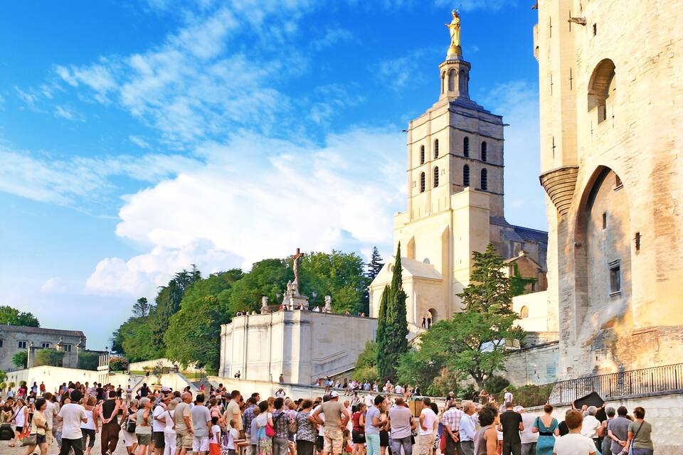 A historic church with a tall bell tower and a crowd of people gathered in front.