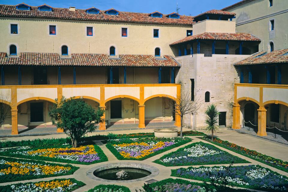 A courtyard with a fountain surrounded by flower beds and arches.