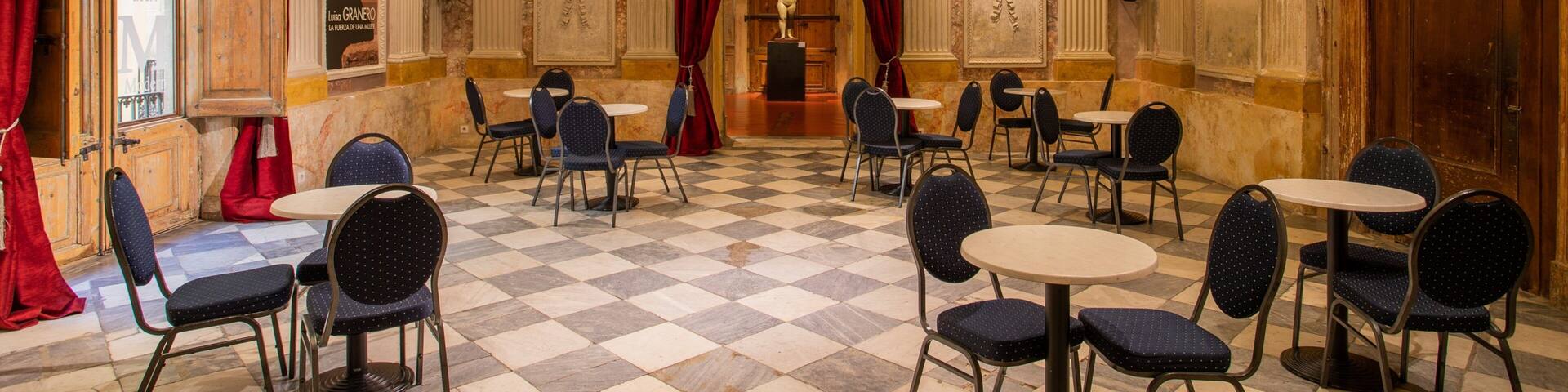 A grand hall with marble floors, ornate columns, and red curtains.