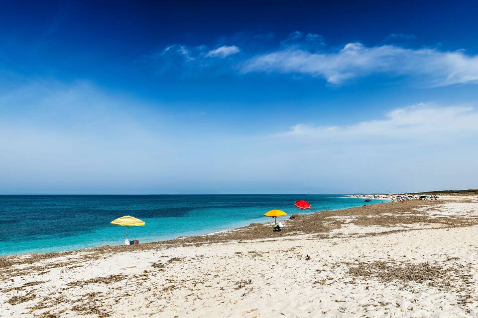 A beach with clear turquoise waters, a sandy shore, and two umbrellas.