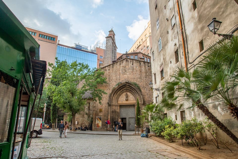 Una calle empedrada con edificios históricos, una iglesia con un arco destacado y palmeras a lo largo del camino.