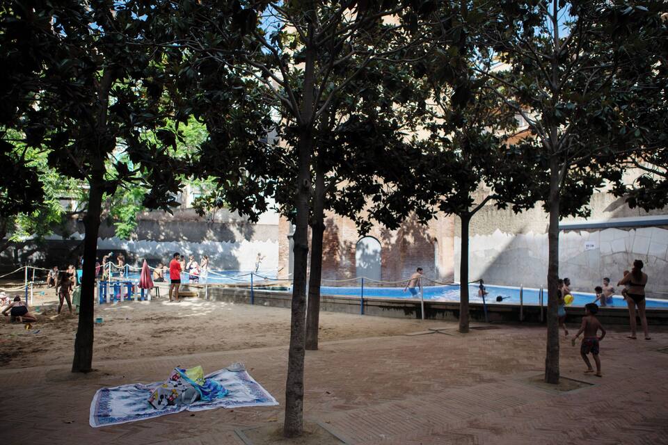 A sandy beach with trees, a volleyball net, and a pool area.