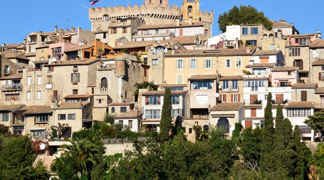 Un pueblo histórico con una estructura imponente que recuerda a un castillo, edificios con tejados de teja anaranjada y abundante vegetación.