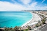 A coastal city with a long beach, clear turquoise waters, and a promenade lined with palm trees.