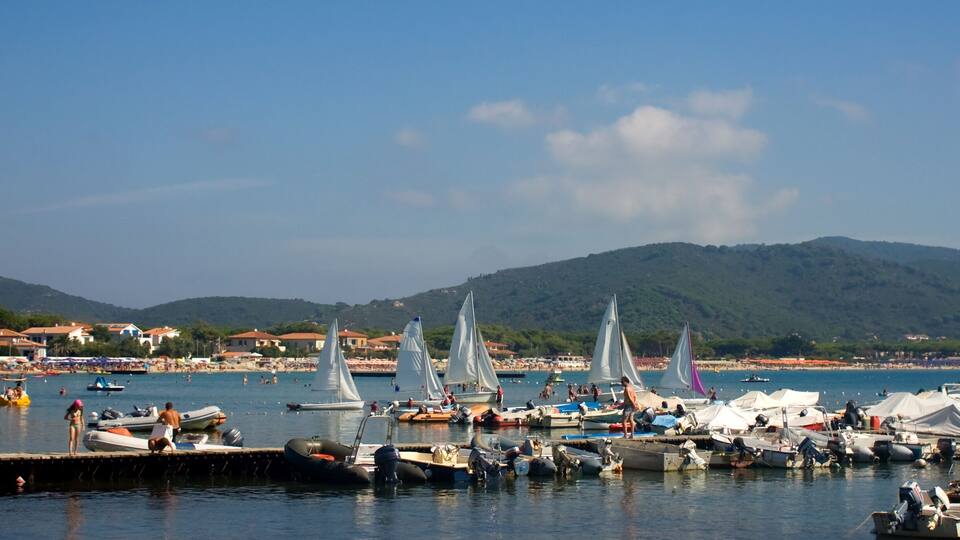 A marina with sailboats, a beach, and mountains in the background.