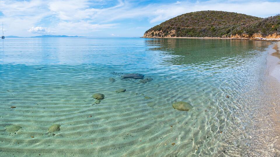 A clear coastal beach with visible sand ripples and a distant boat.