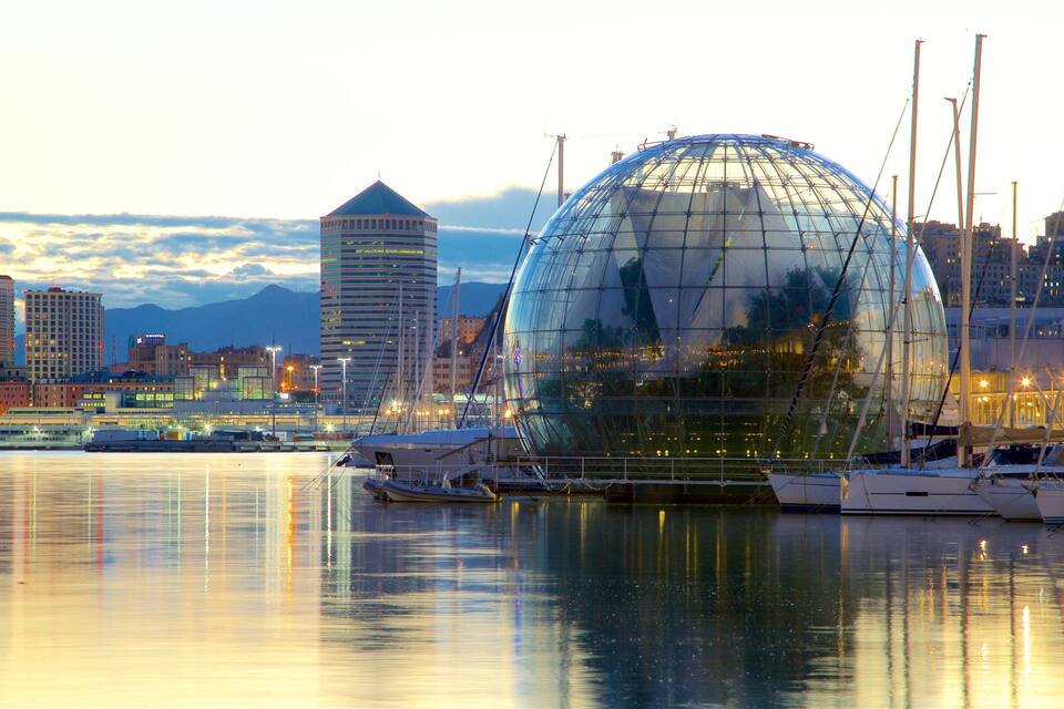 A cityscape with a distinctive glass dome structure reflecting in the water, surrounded by boats and tall buildings.