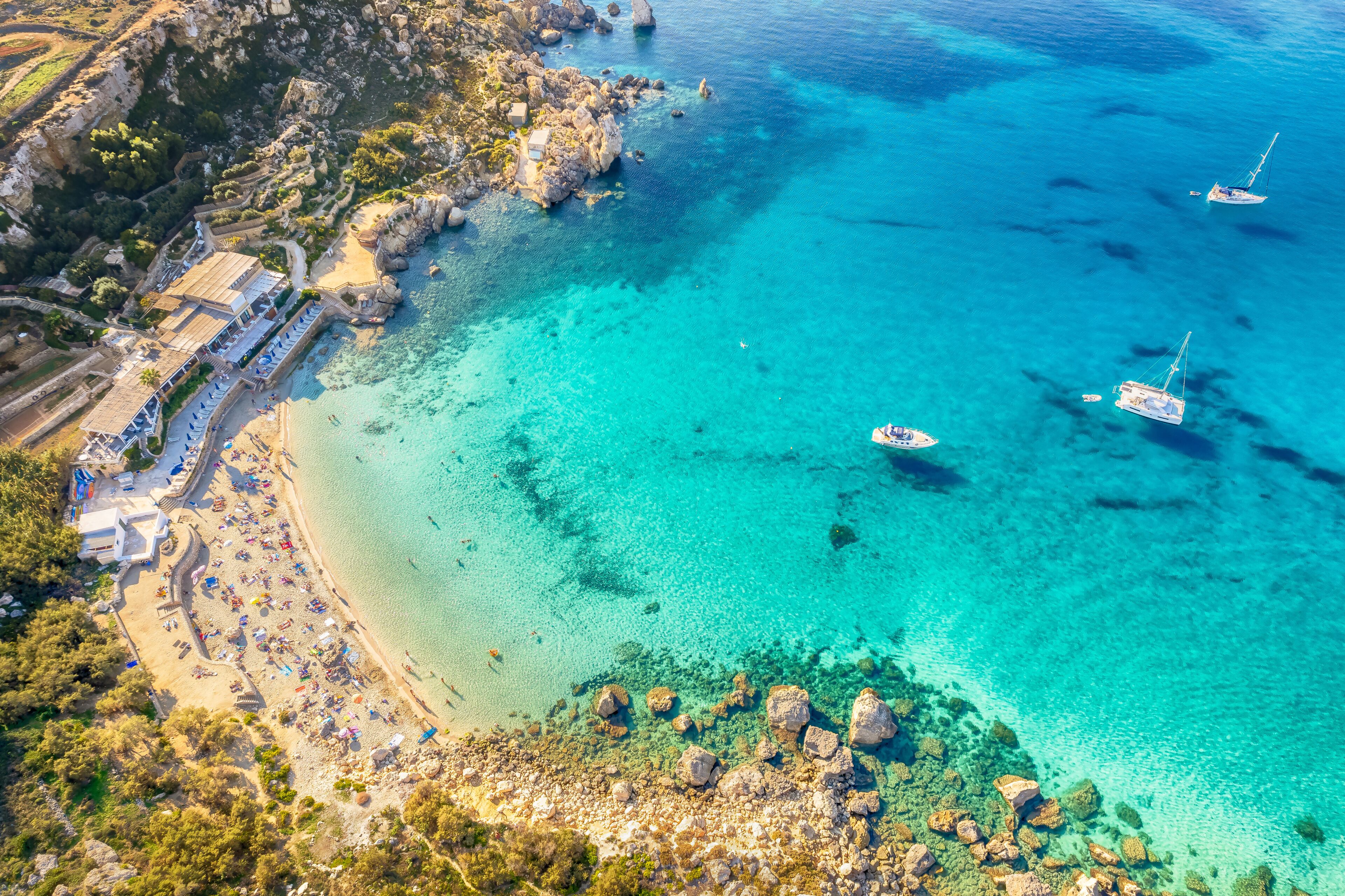 A coastal area with clear turquoise waters, rocky outcrops, and a beach with umbrellas.