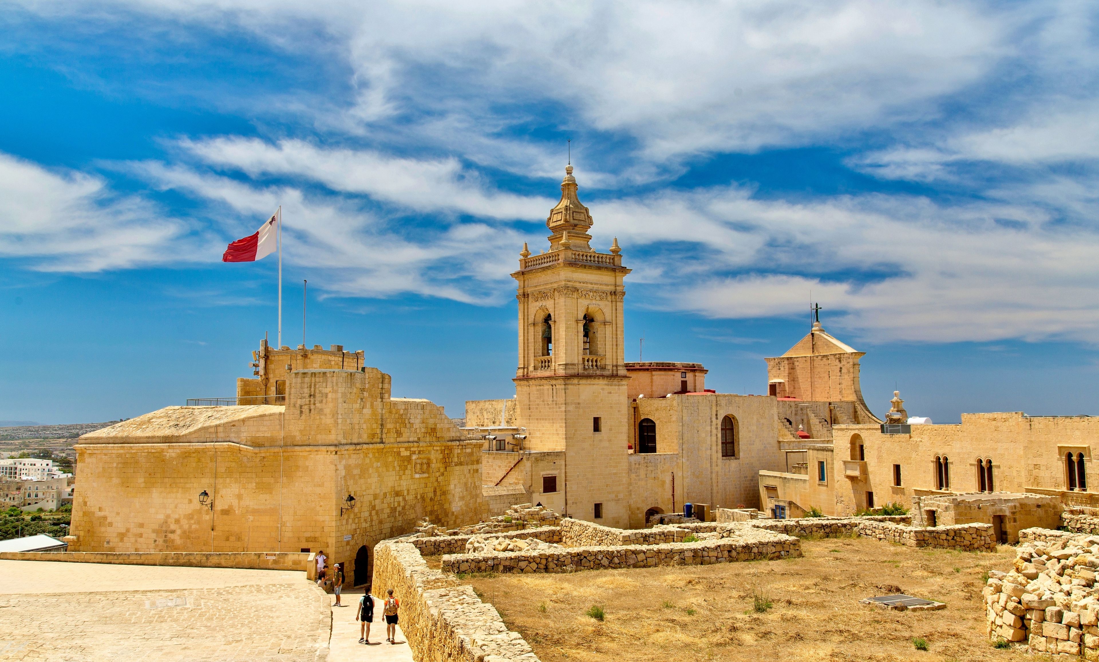 A historic stone fortress with a prominent bell tower and a flagpole with a flag.