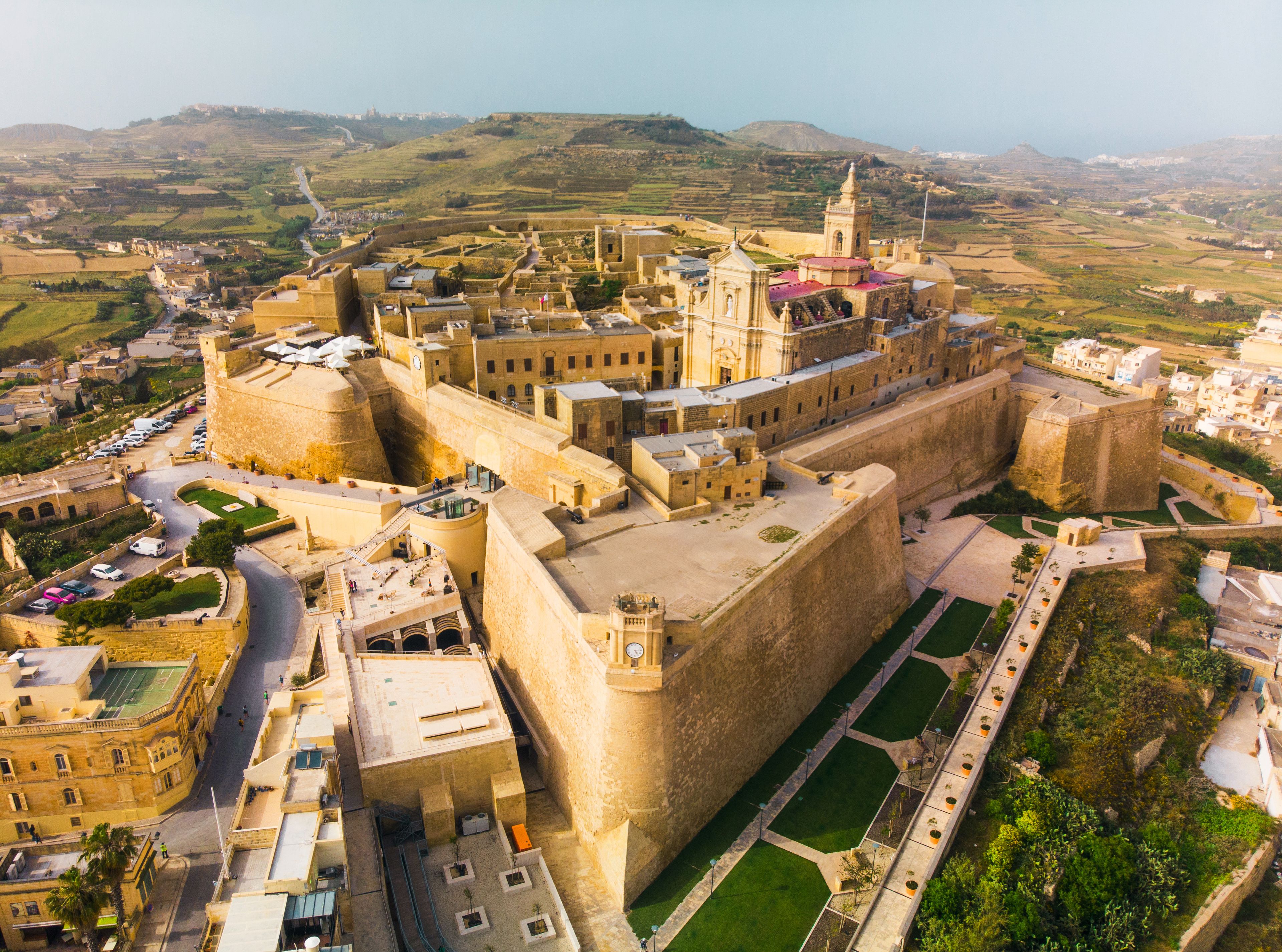 A fortified city with a prominent castle, surrounding walls, and a hilly landscape in the background.