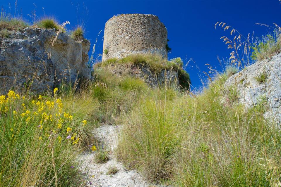 Ein steinerner Turm, umgeben von felsigem Gelände und Wildblumen.