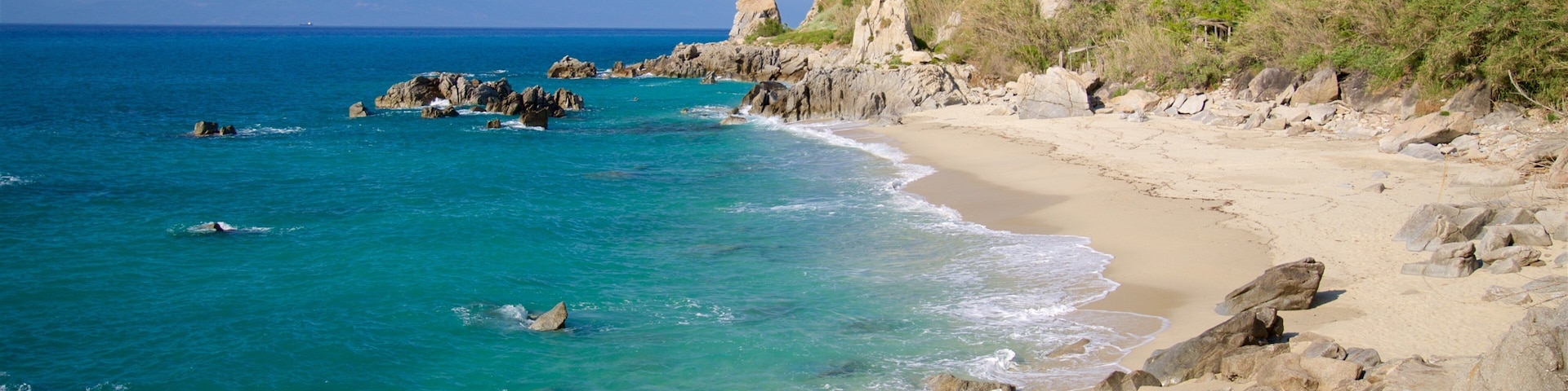 Una costa rocosa con aguas turquesas cristalinas, una playa de arena y una ladera cubierta de hierba.