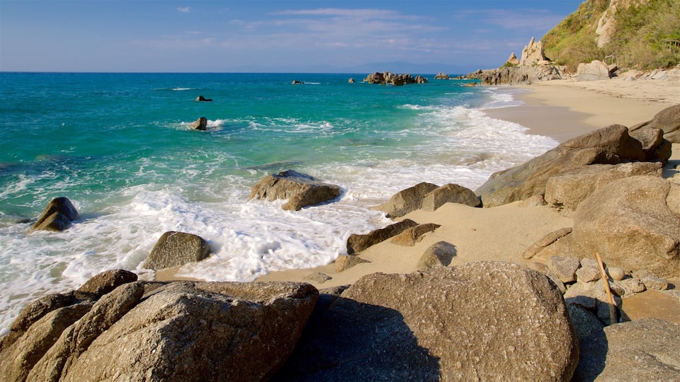 A rocky beach with waves crashing onto the shore and a clear blue sky.
